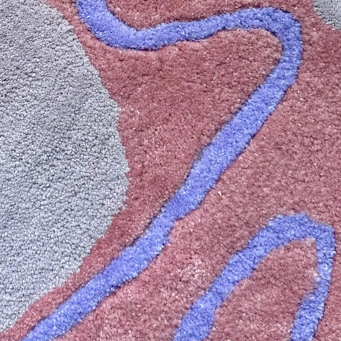 Close-up of a tufted rug with wavy purple lines on a pink and lilac background