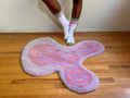 Pink and purple abstract rug on a wooden floor with a person wearing colorful socks.