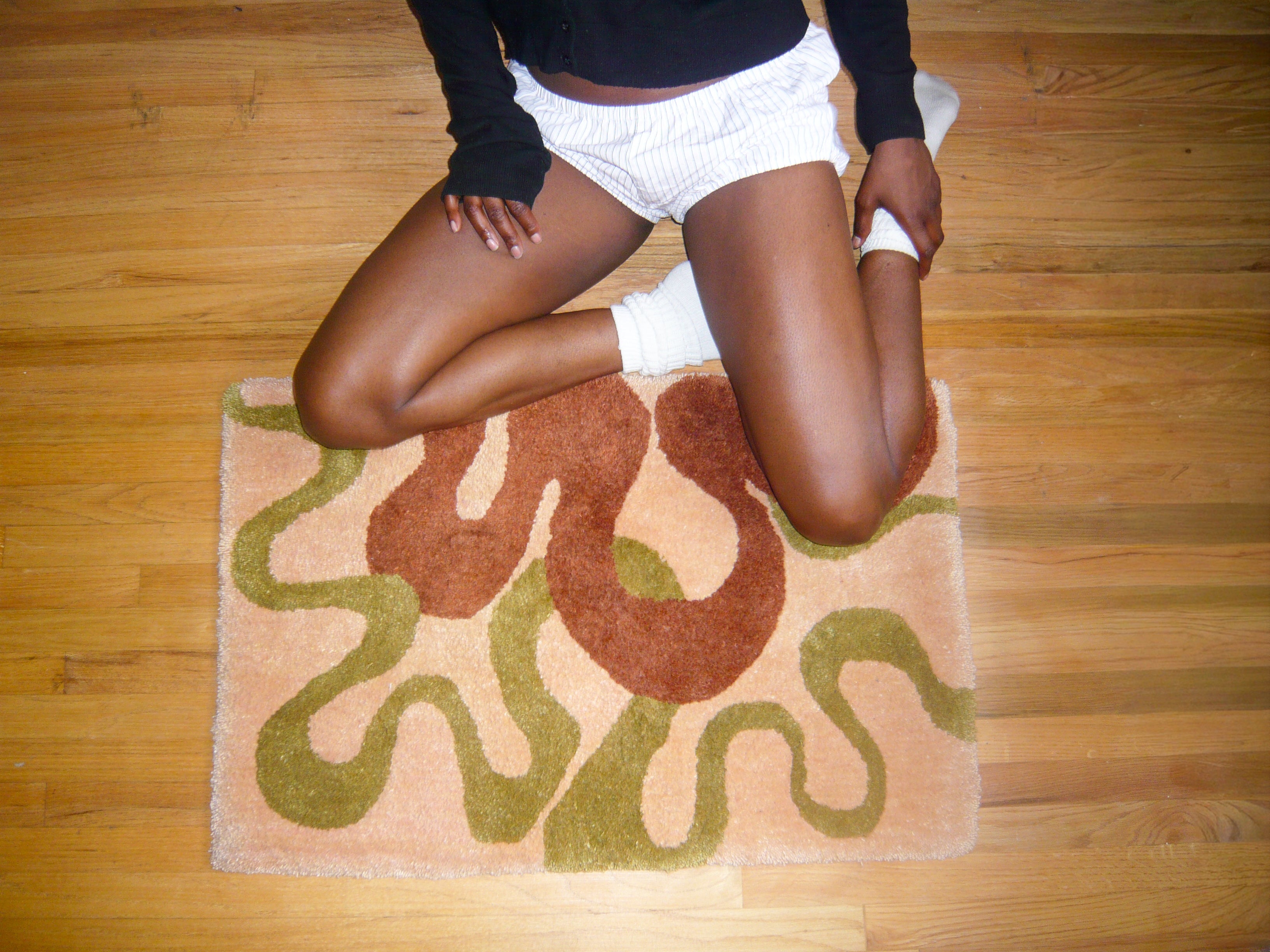 Person sitting on a patterned rug with wooden floor background