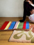 Colorful hand tufted rug with a rainbow pattern on a wooden floor.